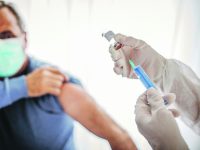 Two people, medical doctor in protective suit giving a senior male Covid-19 coronavirus vaccine.