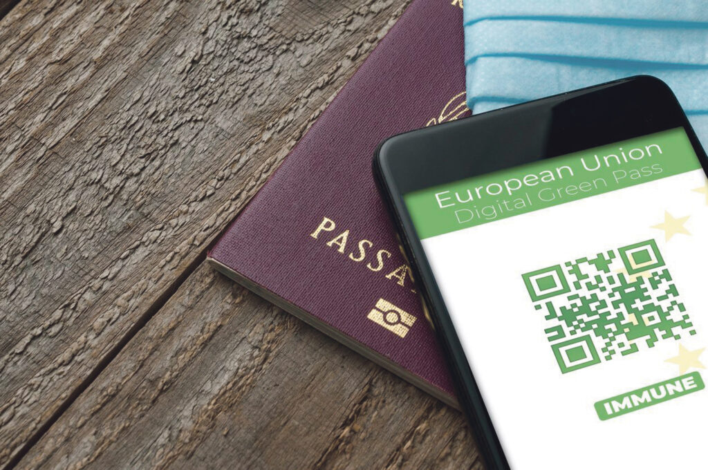 Digital Green Pass concept: Smartphone over a passport and a surgical mask on a wooden table show an hypotetical app for the Digital Green Passport (or digital pass certificate) (Digital Green Pass concept: Smartphone over a passport and a surgical ma