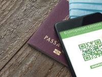 Digital Green Pass concept: Smartphone over a passport and a surgical mask on a wooden table show an hypotetical app for the Digital Green Passport (or digital pass certificate) (Digital Green Pass concept: Smartphone over a passport and a surgical ma