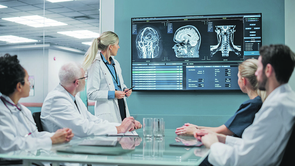 Hospital Conference Meeting Room: Female Neurologist Shows MRI Scan Brain Images on TV Screen, Team of Neuroscientists, Doctors Discuss Patient Treatment, Drug Research, Medicine Development