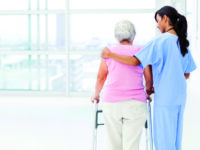 Rear view of female nurse assisting senior woman with walker in nursing home. Horizontal shot.