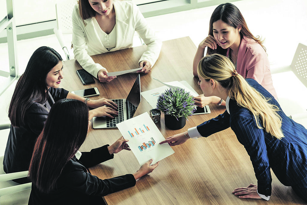 Businesswoman in group meeting discussion with other businesswomen colleagues in modern workplace office with laptop computer and documents on table. People corporate business working team concept.