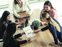 Businesswoman in group meeting discussion with other businesswomen colleagues in modern workplace office with laptop computer and documents on table. People corporate business working team concept.