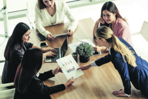 Businesswoman in group meeting discussion with other businesswomen colleagues in modern workplace office with laptop computer and documents on table. People corporate business working team concept.