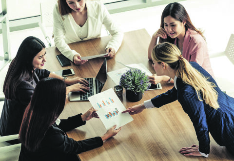 Businesswoman in group meeting discussion with other businesswomen colleagues in modern workplace office with laptop computer and documents on table. People corporate business working team concept.