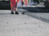 Road workers in protective clothing are repairing the asphalt surface of the streets with hot asphalt, close-up on the workers' feet, slow motion
