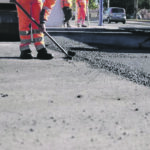 Road workers in protective clothing are repairing the asphalt surface of the streets with hot asphalt, close-up on the workers' feet, slow motion