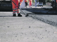 Road workers in protective clothing are repairing the asphalt surface of the streets with hot asphalt, close-up on the workers' feet, slow motion