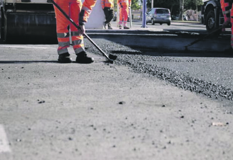 Road workers in protective clothing are repairing the asphalt surface of the streets with hot asphalt, close-up on the workers' feet, slow motion